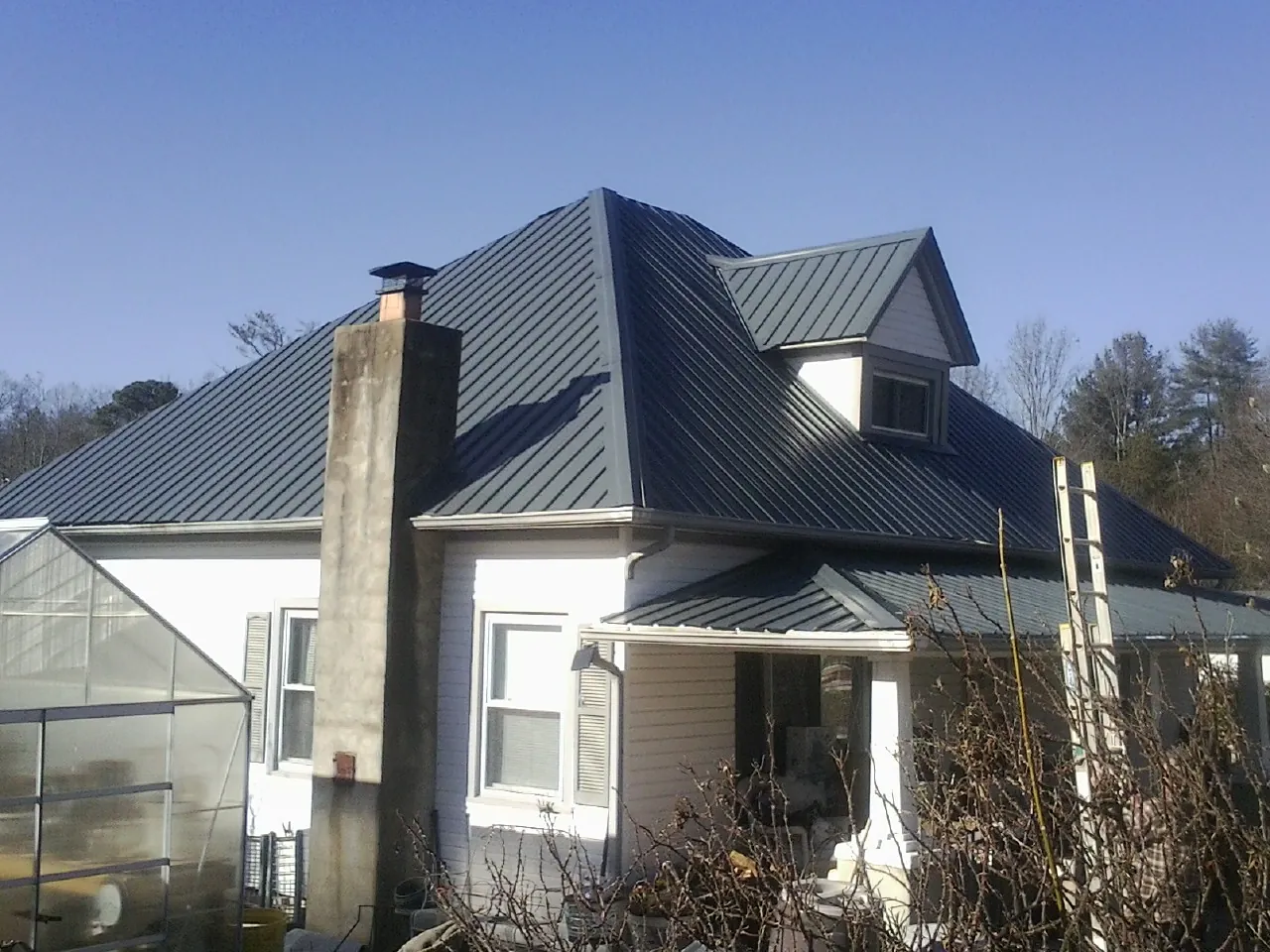 Dark blue standing seam metal roof on a white farmhouse with dormer — Slate & Tile Roof Repair by Roofing Brothers in Nova