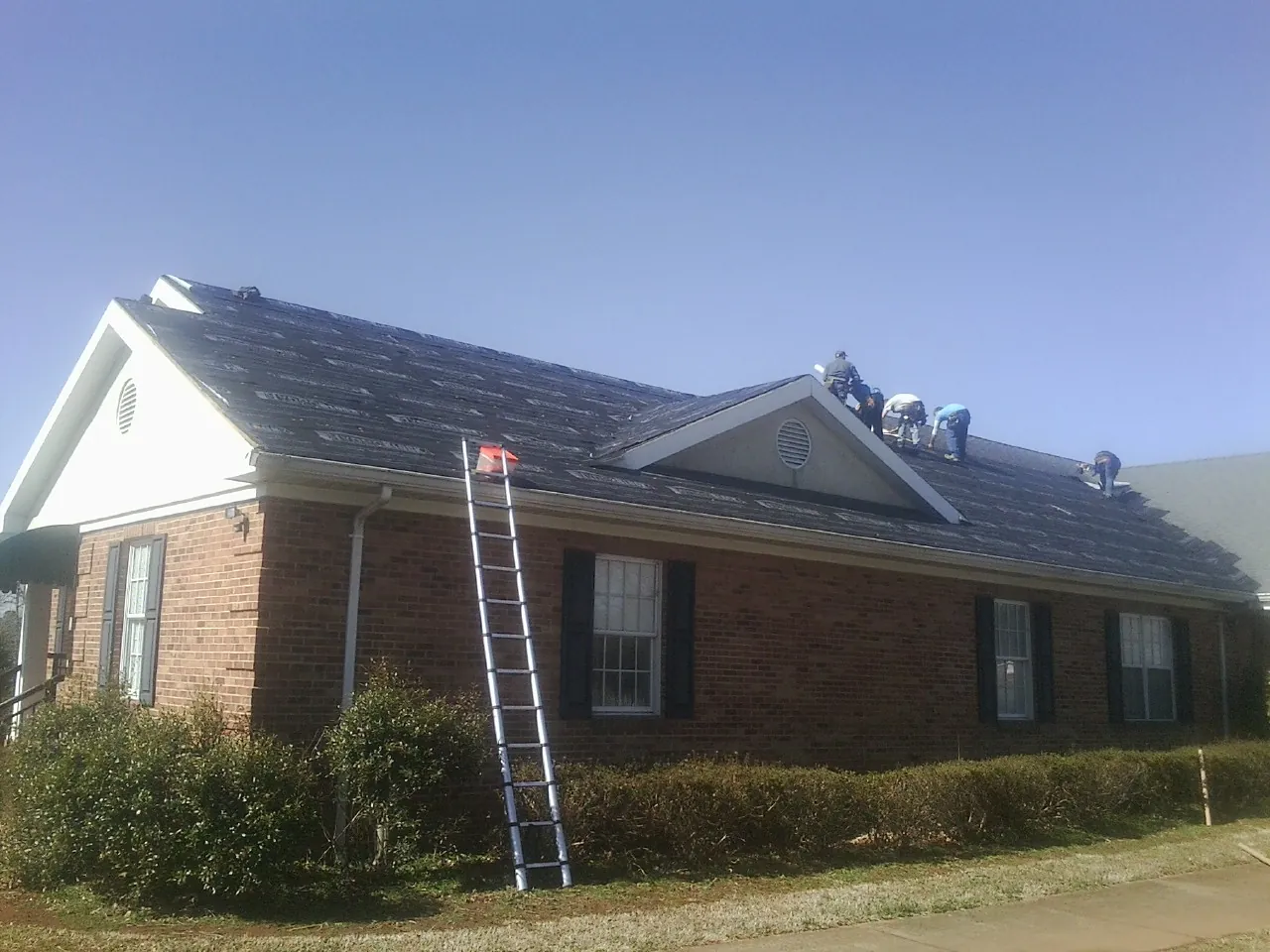 Crew tearing shingles off a brick ranch roof with a ladder set — Metal Roof Repair work by our crew in Nova
