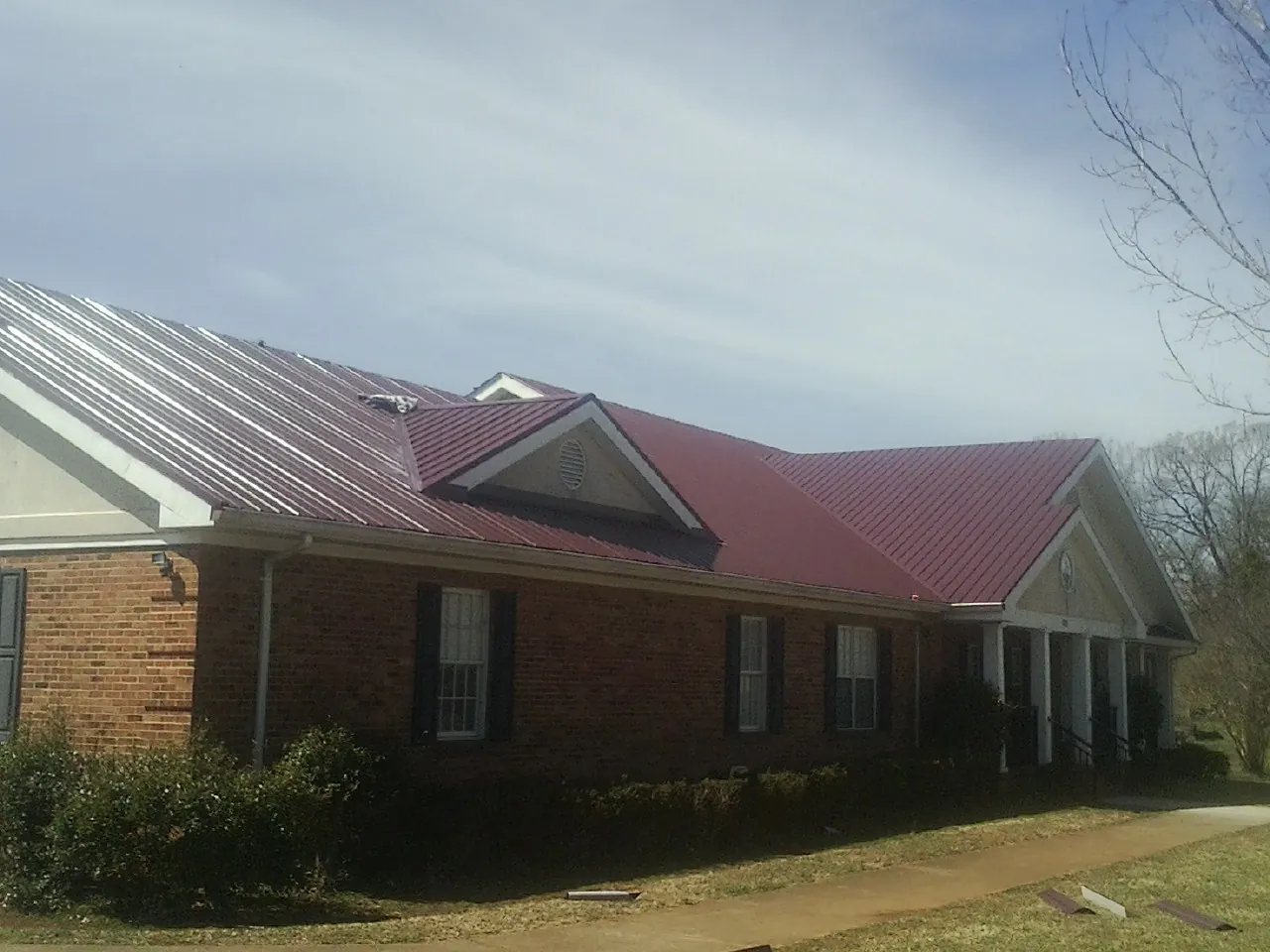 Red metal roof with gabled entries on a long brick building, from a Hail Damage Roof Repair job in Nova