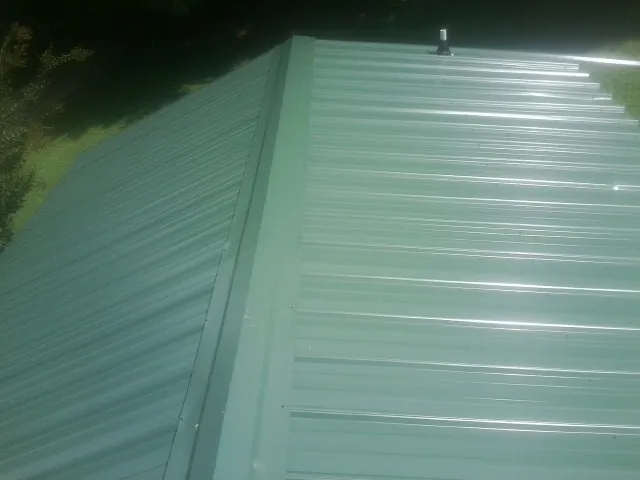New green metal panels meeting at the ridge of a roof — Flat Roof Repair work by our crew in Nova