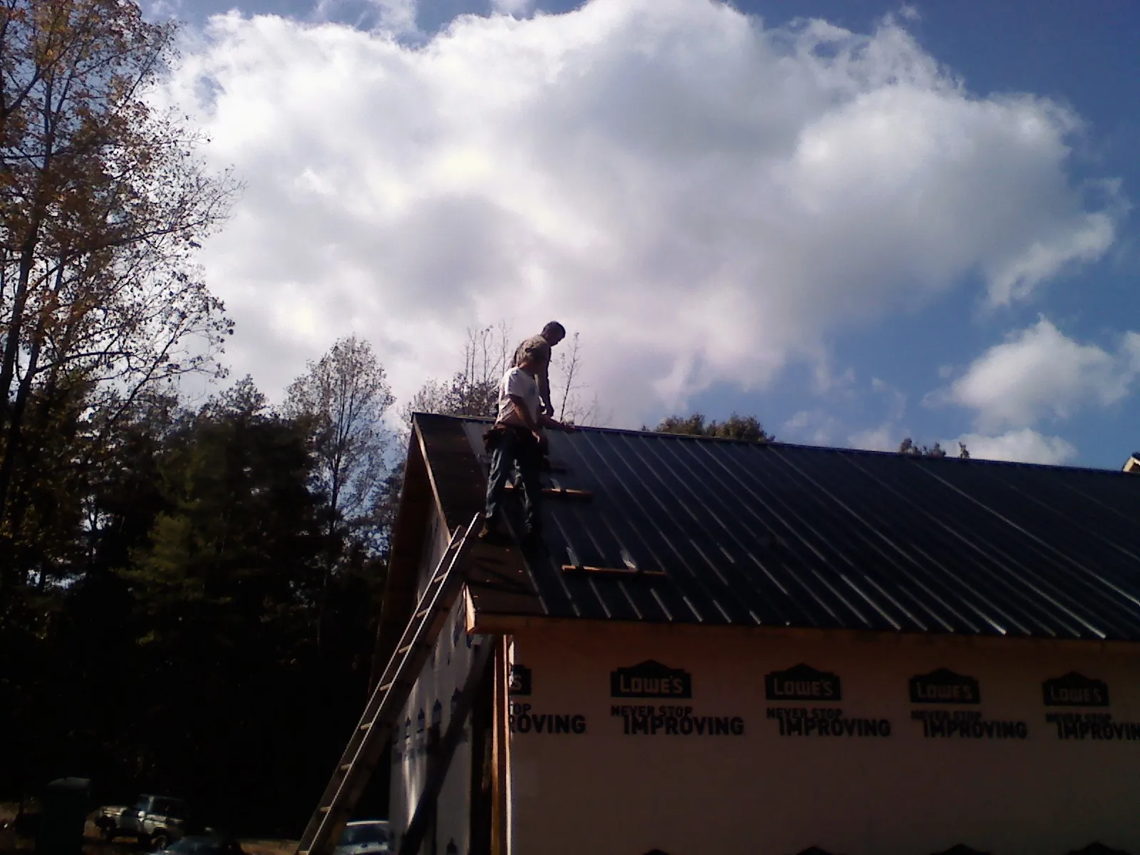 Roofer fastening dark metal panels high against a cloudy sky, from a Roof Inspection job in Nova